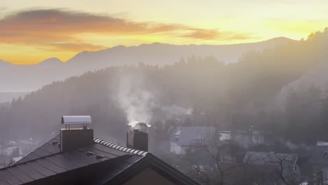 smoke rising from a chimney on a house in winter with sunset in the background