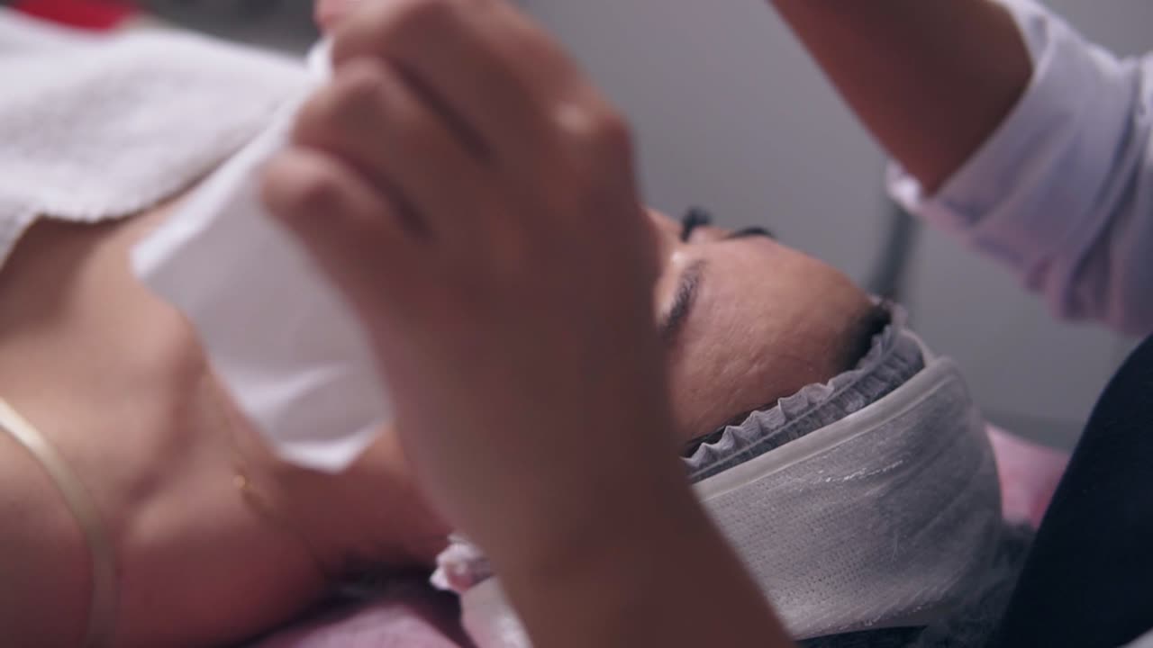 Close Up view of professional cosmetologist dab dry woman's clean face skin using paper tissue. Young woman is lying on the couch