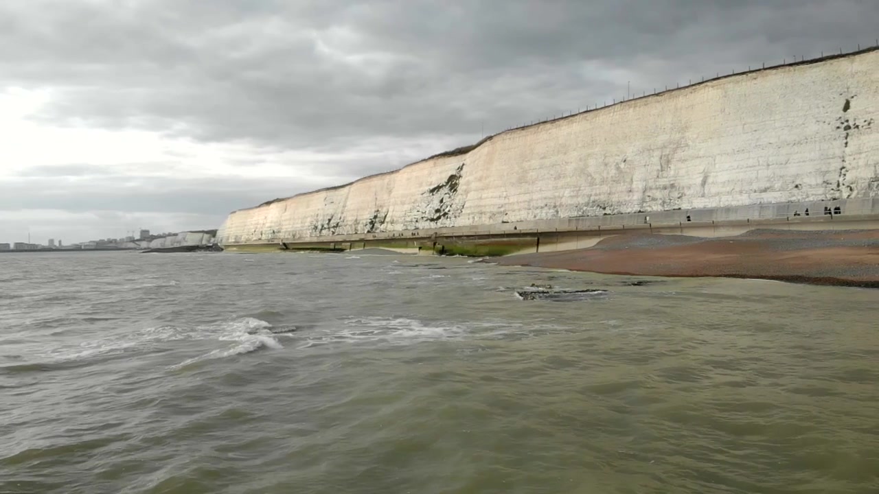 Ripresa al rallentatore che rivela le bianche scogliere di Rottingdean con le onde che lambiscono la riva.