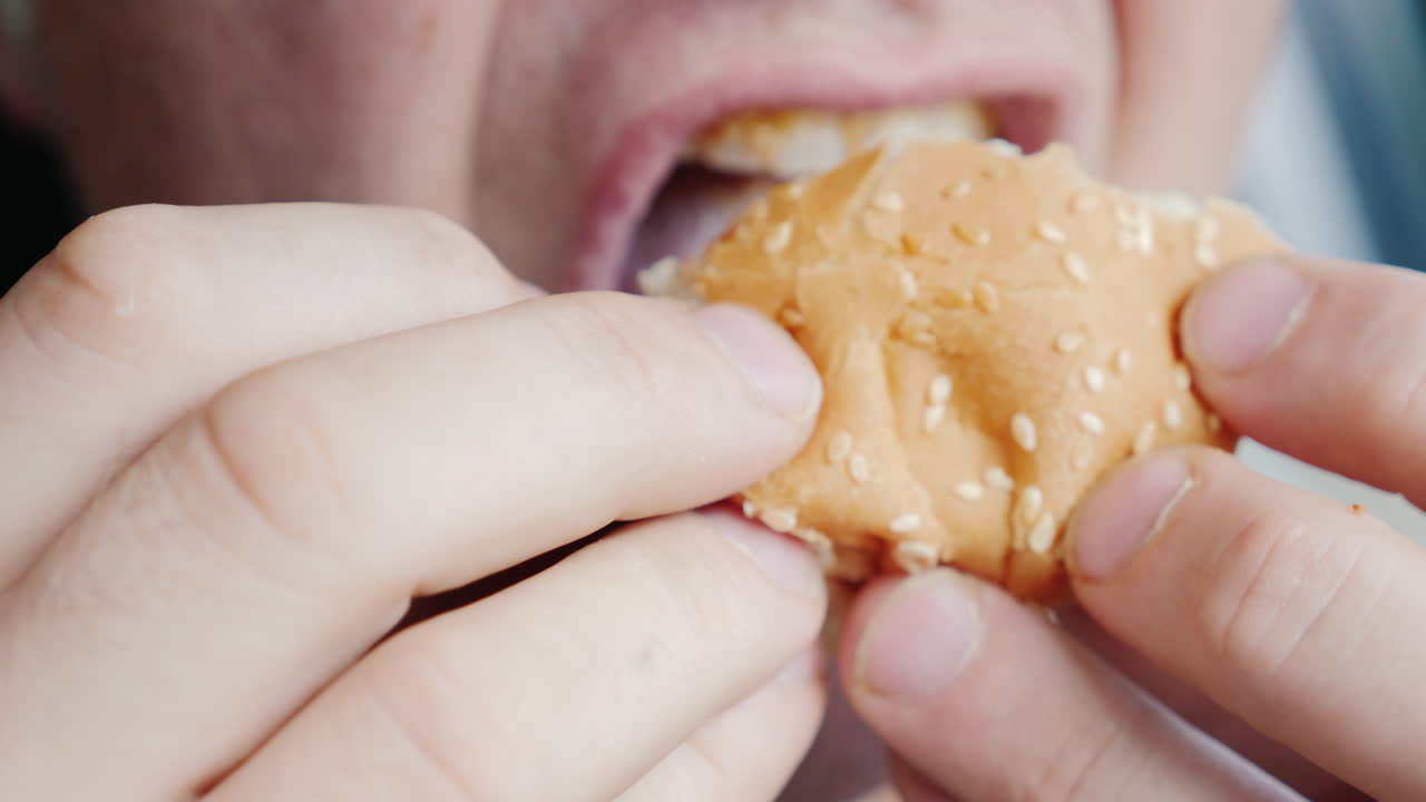 un hombre hambriento come ansiosamente una hamburguesa solo su boca es visible en el marco
