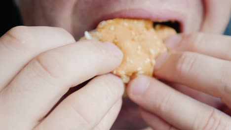 a hungry man eagerly eats a hamburger only his mouth is visible in the frame