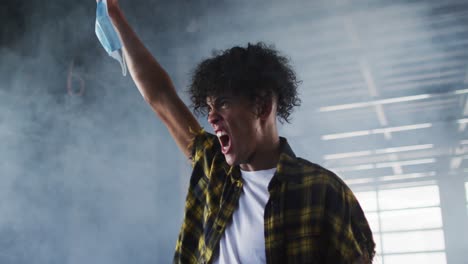 mixed race man protesting while holding protest face mask in the air