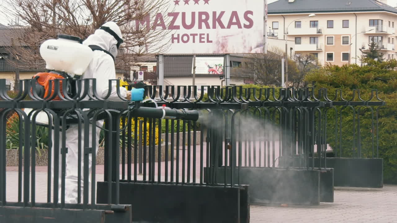 Person in hazmat suit disinfecting a fence in front of a hotel