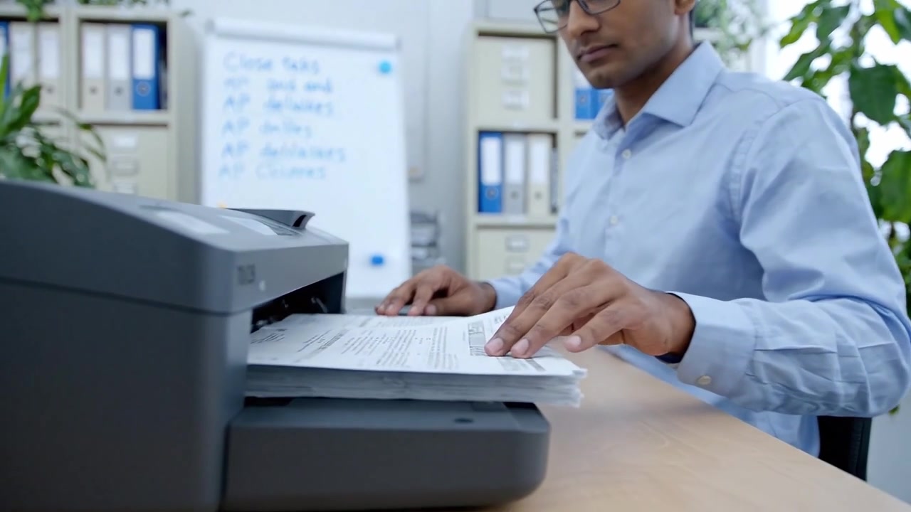 Focused individual working diligently at a desk using a printer in a modern office environment, highlighting productivity and efficient document management.