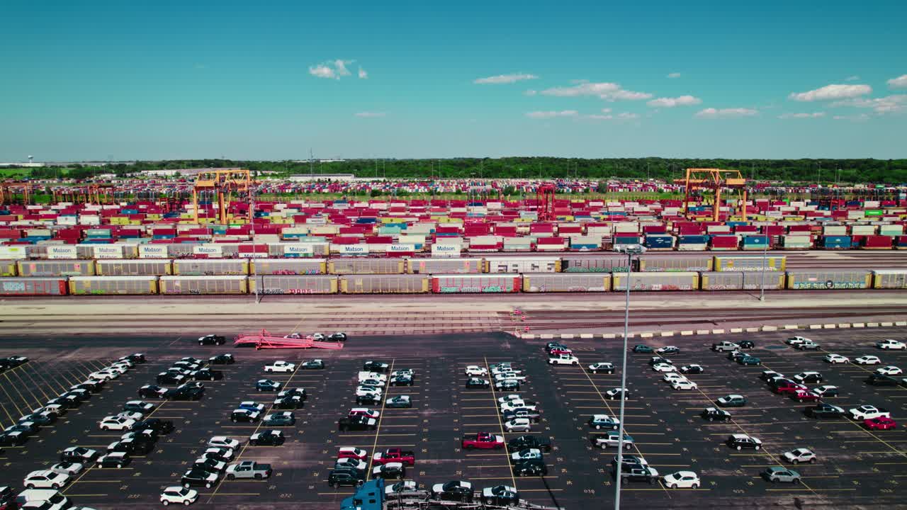 The parking lot with new cars at a car hauling company, containers and cranes in the background.