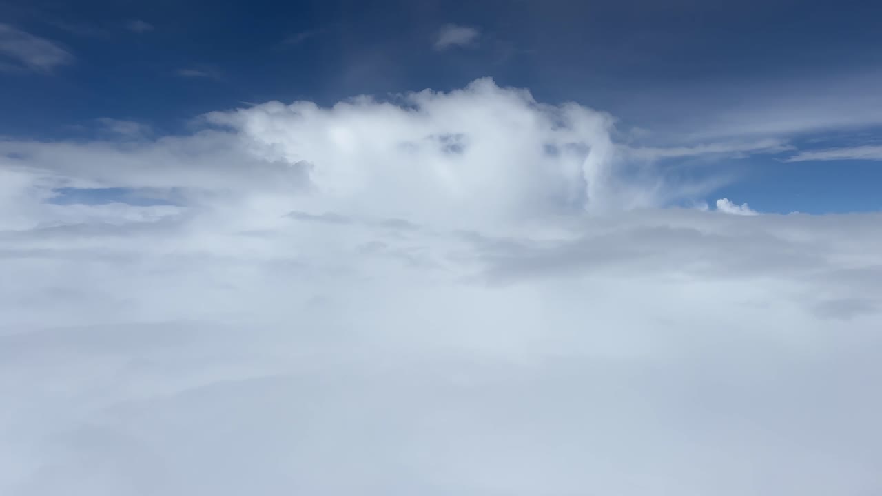 A peaceful aerial scene showing moving clouds and blue sky from an airplane window. Soft layers pass beneath the aircraft, creating a calm and cinematic view during flight