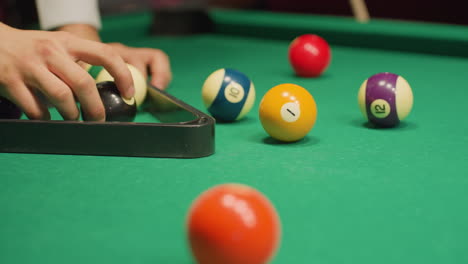 person hand carefully places billiard balls into triangle rack on green pool table, aligning them for perfect setup before break shot. close-up shot highlights precision, focus, and strategic game