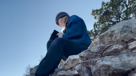 low angle of a person sitting on a mountain writing in a notebook