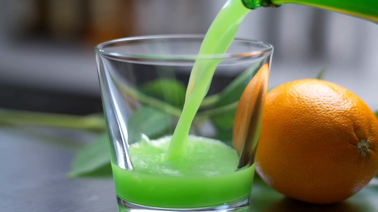 Primo piano di una bevanda verde versata in un bicchiere, una vivace bevanda verde lime che scorre da una bottiglia in un bicchiere trasparente.