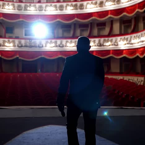 actor on classic theatre stage. man is speaking in spotlights during the performance. back view video