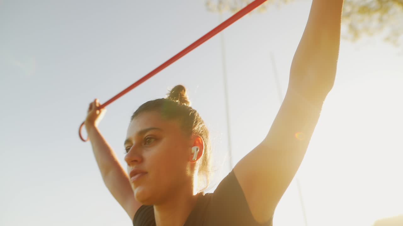Woman working out with resistance band and dumbbells in the sun