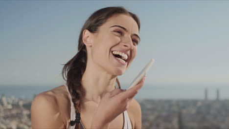 Portrait-of-smiling-woman-recording-voice-message-on-mobile-phone-at-street