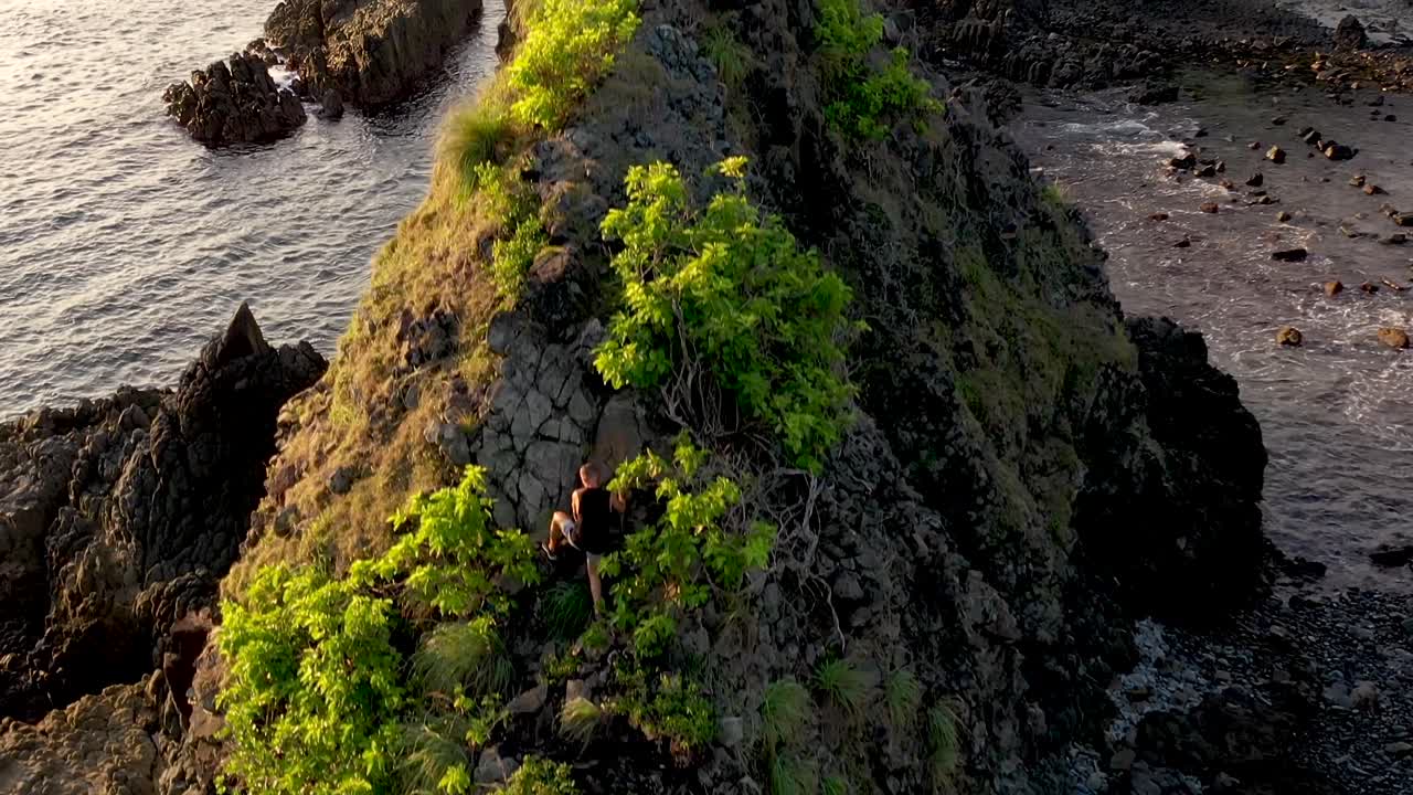 Adventurous man free climbing on the rock elevated on the sea