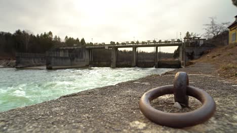 flowing water of the bavarian river isar with a dam in the background and a mooring metal ring focused as foreground element