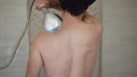 white man with dark hair washes his back with the shower head