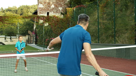 rear view of a man playing tennis with his teen son on a sunny summer day