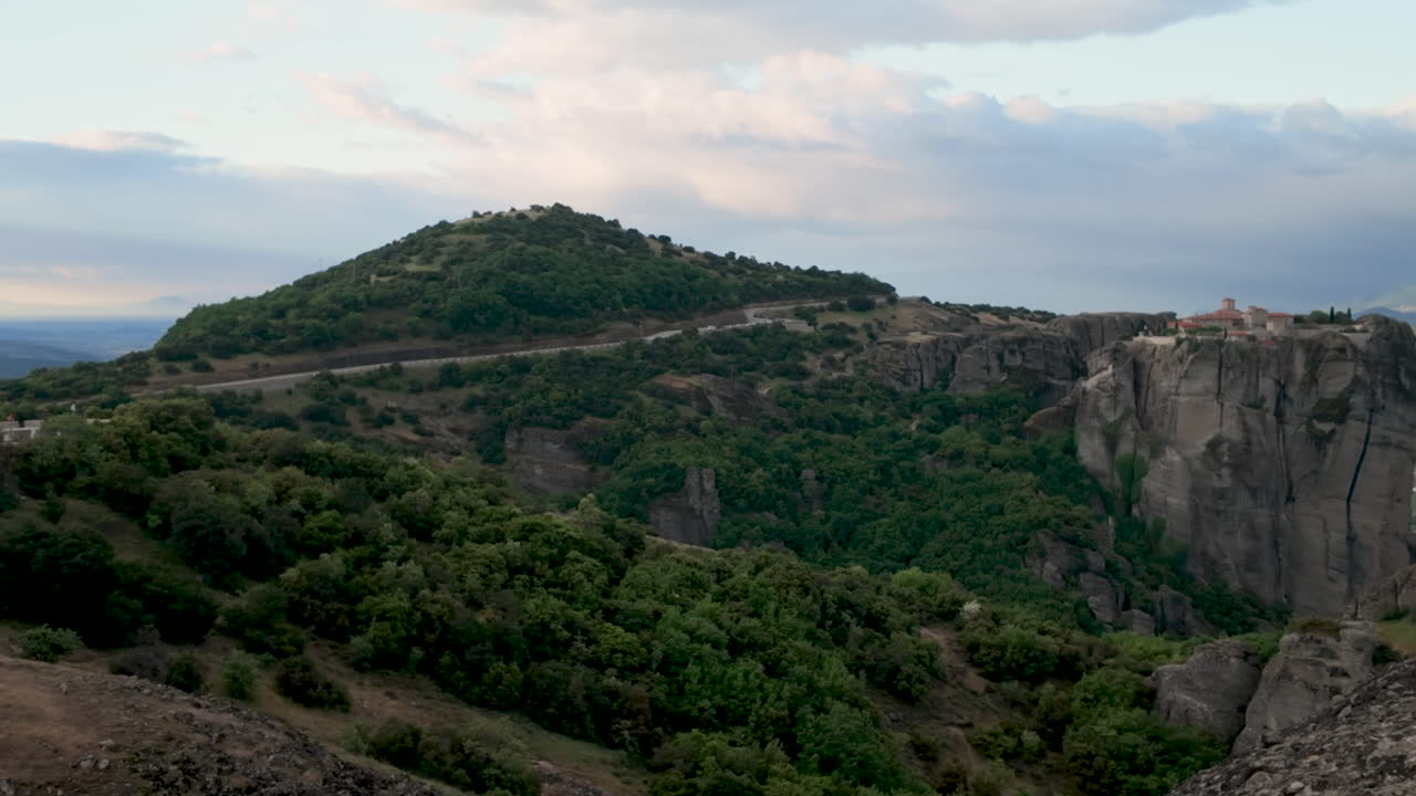 Vista mozzafiato del monastero di Meteora arroccato su una spettacolare formazione rocciosa, circondato da lussureggianti colline verdi e montagne lontane in Grecia