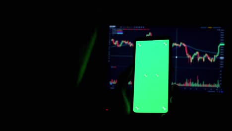 a trader holds a smartphone with a green screen in hands in a dark room. 4k