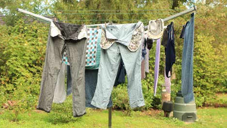 Laundry-gently-waving-in-a-breeze-hanging-to-dry-in-a-garden-on-a-foldable-rotating-drying-rack-with-lines-and-cords-against-a-natural-greenery-background