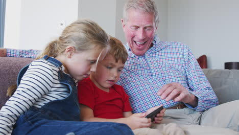 Grandfather-Playing-Video-Game-With-Grandchildren-On-Mobile-Phone-At-Home