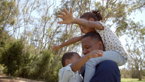 Mixed-race-dad-carrying-his-two-kids-in-the-park