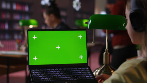estudiante usando una computadora portátil con pantalla verde en una biblioteca