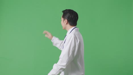 side view of asian male doctor with stethoscope waving hand and smiling while walking on green screen background in the hospital