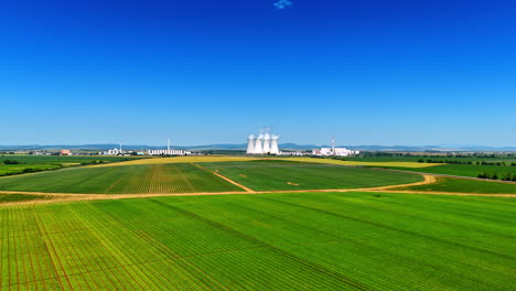 beautiful green fields in the countryside. white smoke comes out of cooling towers of the plant at backdrop.