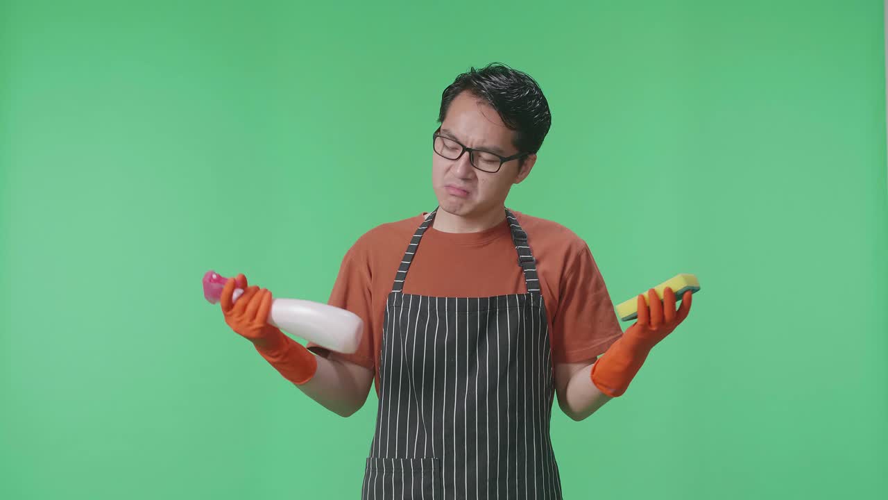 아시안 남성 집주인이 앞옷을 입고 스프레이와 부 스폰지를 버리고 녹색 스크린 스튜디오에서 팔을 교차합니다.