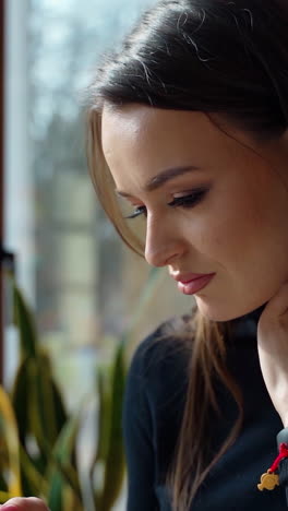 side view of a lovely woman with a phone indoors. young beautiful girl sitting in a cafe and looking into her mobile phone. vertical video