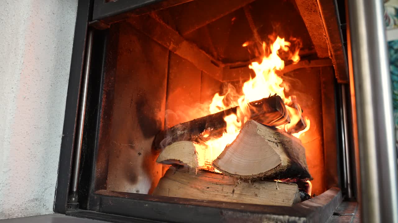 Slow motion view of bright flames dancing over burning logs inside a fireplace. Warm glow and natural fire movement create a cozy and relaxing indoor home atmosphere