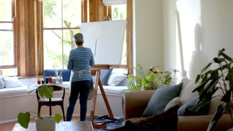 Mujer-Birracial-Mayor-Usando-Delantal-Y-Pintando-Sobre-Lienzo-Grande-En-Casa,-Cámara-Lenta