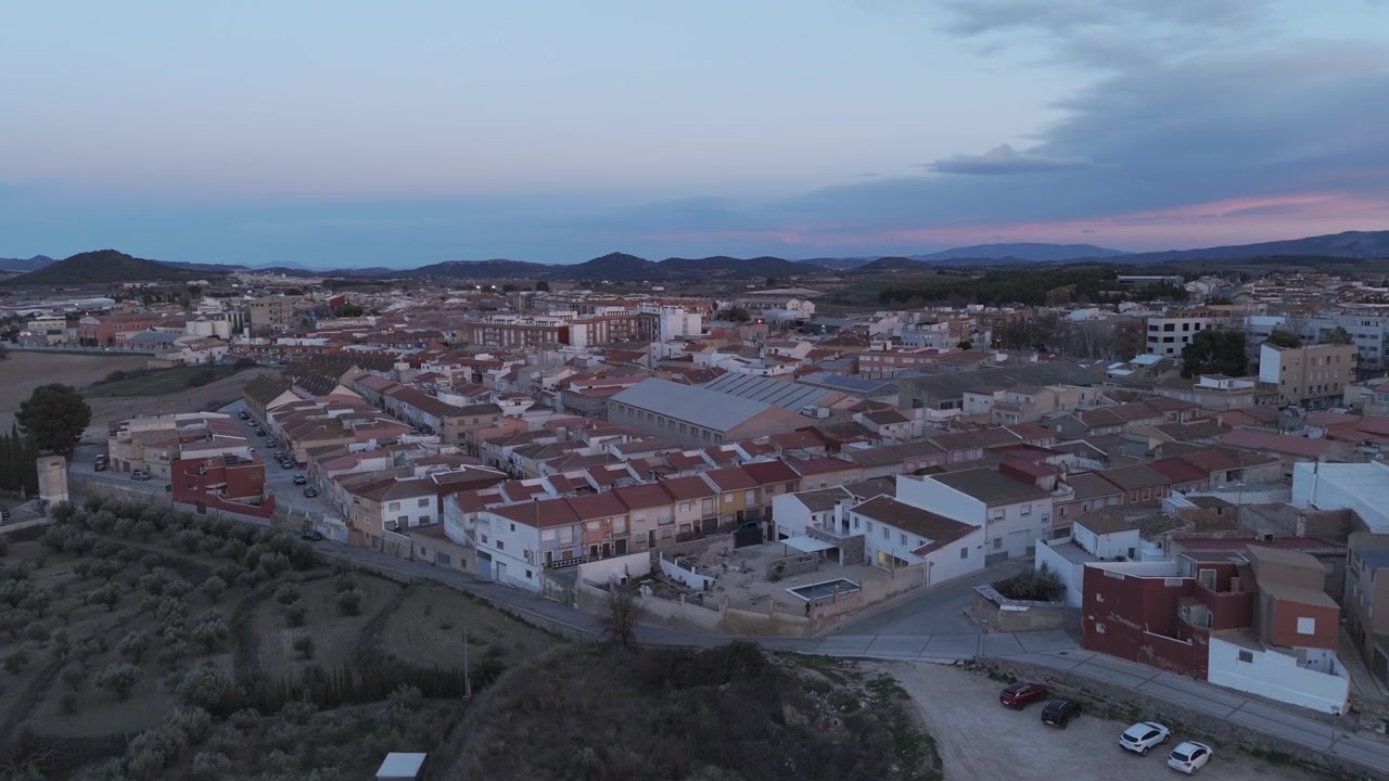 Movimento laterale del drone che rivela la città di Bullas al tramonto con cieli rosa, campi rurali e montagne distanti a Murcia