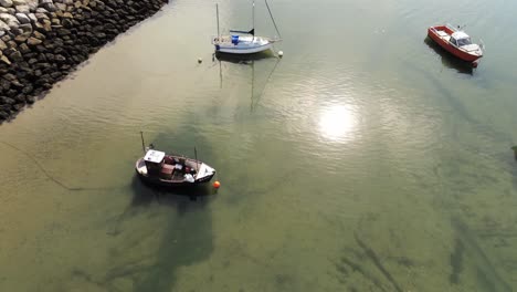 aerial birdseye above boats in shimmering sunny patterned sand beach at low tide marina pull back slow