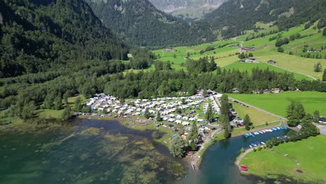 camping area filled with white vans holiday area spot to get away for a family trip in pure nature bird view great mountains in the background houses on different places scattered boats on water cars