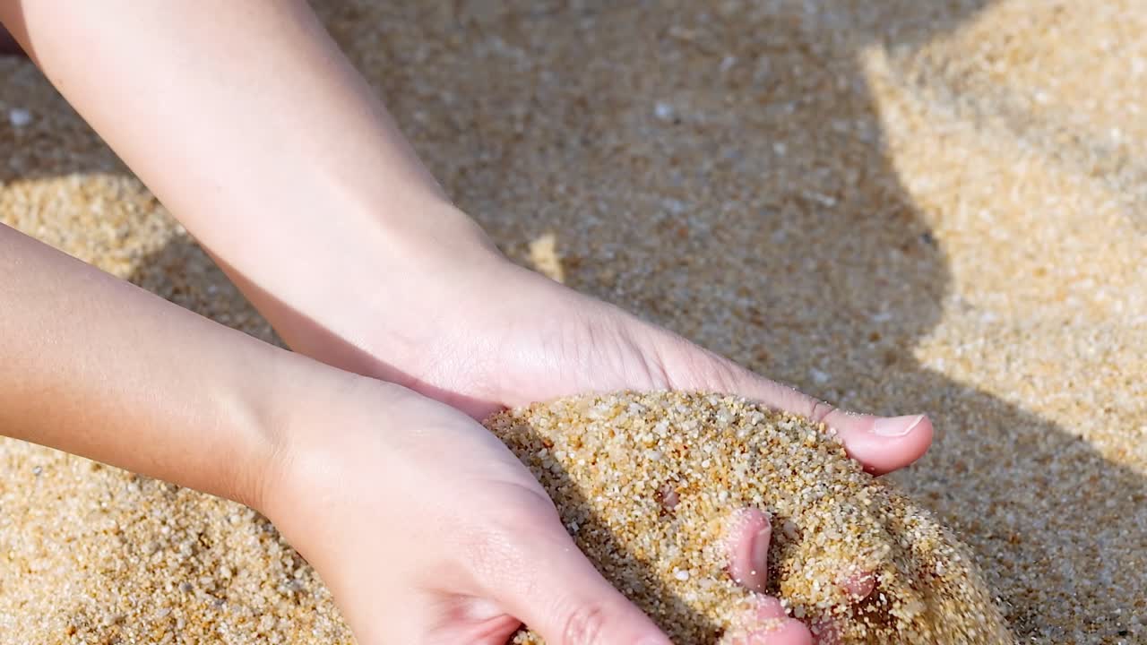 Close-up of hands delicately sifting and pouring golden sand, capturing the texture and movement.