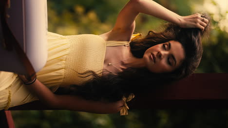 beautiful young brunette woman wearing yellow summer dress, combing hair back with hand, camera tracks in, close up portrait, cinematic slow motion, vertical