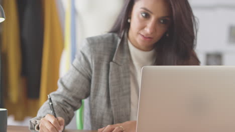 female fashion designer in studio working on laptop computer