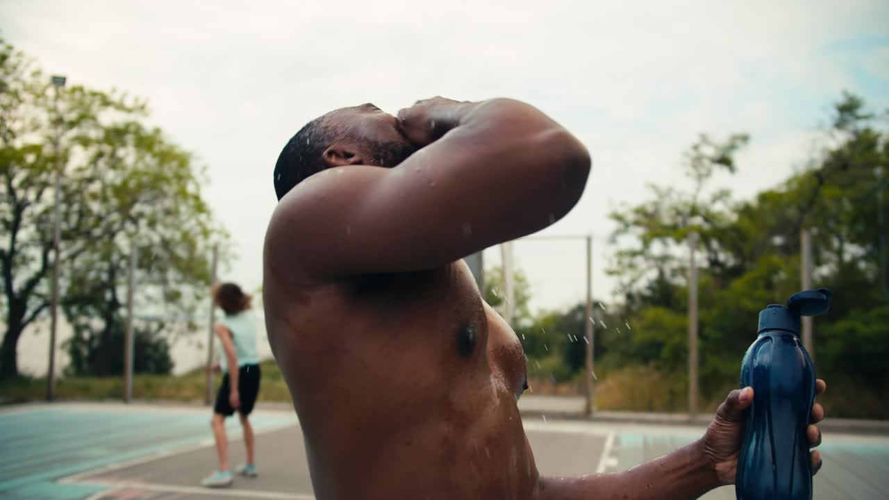 un hombre de piel negra después de jugar al baloncesto se vierte agua en la cabeza de una botella especial para enfriarse y grita su grito de batalla en la cancha de baloncesto