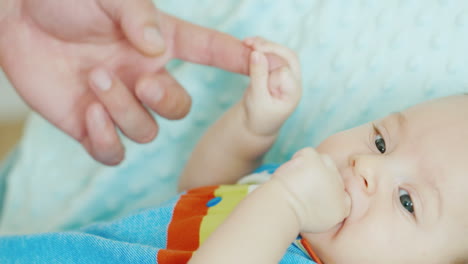 bebé sosteniendo el dedo de su padre niño sereno de dos meses acostado en la cama