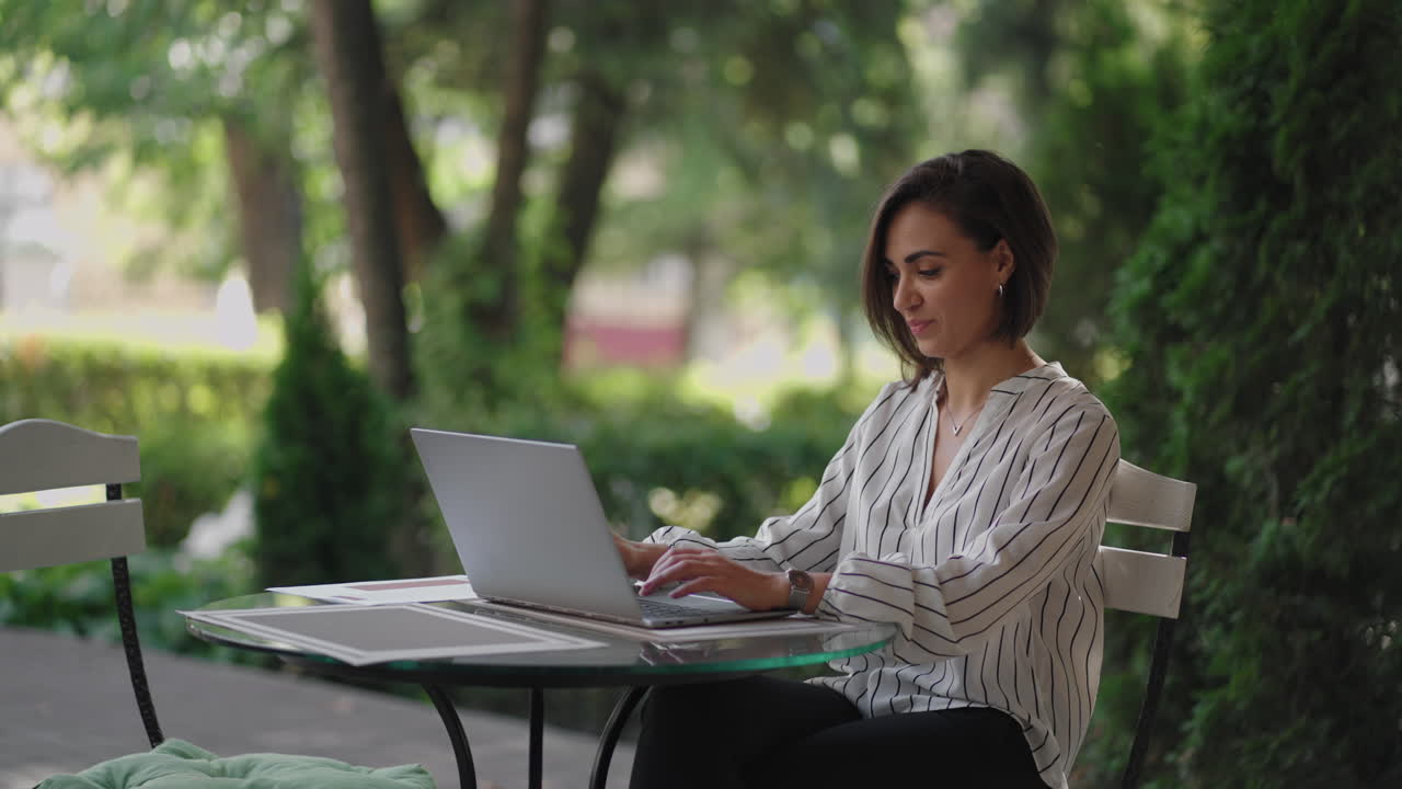 Business Woman Brunette arabic Hispanic ethnic group is typing on a laptop while sitting at a table in a summer cafe doing remote work. Freelancer woman. Small business