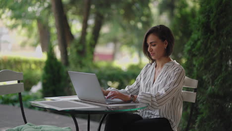 Business-Woman-Brunette-arabic-Hispanic-ethnic-group-is-typing-on-a-laptop-while-sitting-at-a-table-in-a-summer-cafe-doing-remote-work.-Freelancer-woman.-Small-business