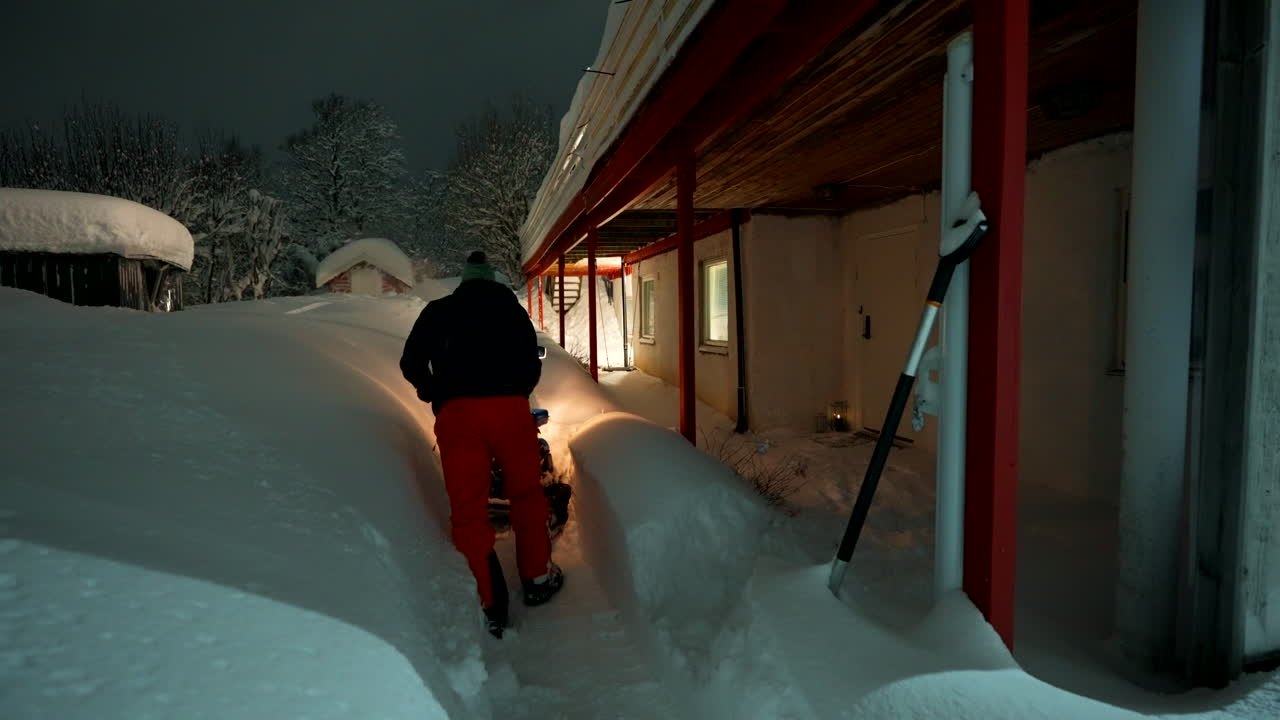 A man walks on path using snowplows to clear area on side of building, Norway’s snowy urban winter setting