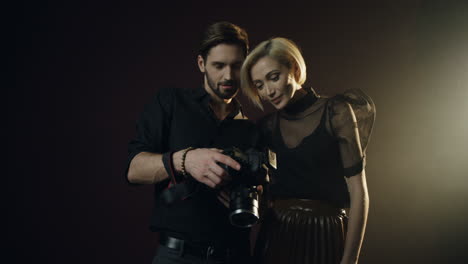 photographer man showing photos of photoshoot to the young blond woman model on the camera screen in the dark studio