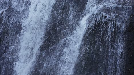 Slow-motion-rushing-large-waterfall-sliding-down-a-rocky-wall