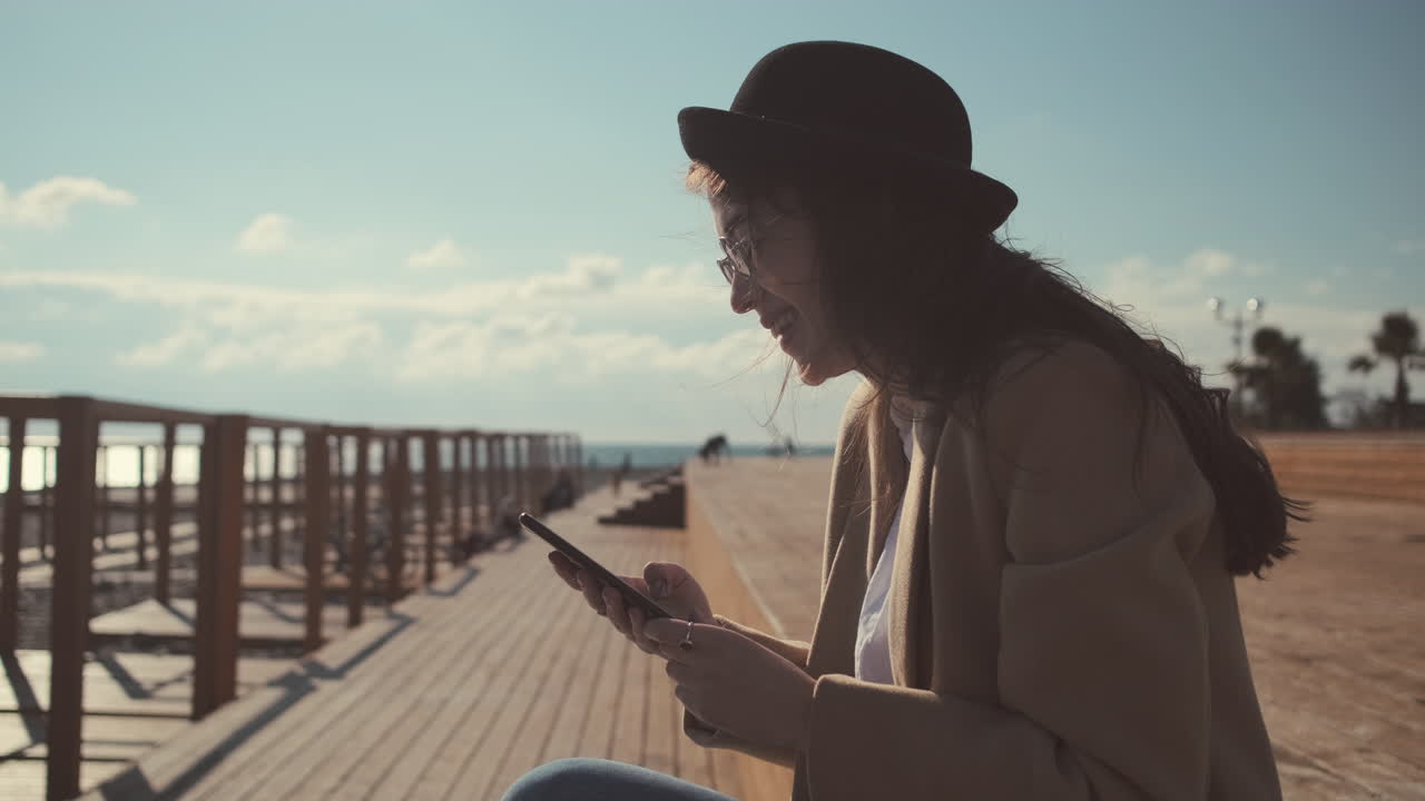 Plaj iskelesinde akıllı telefon kullanan genç kadın
