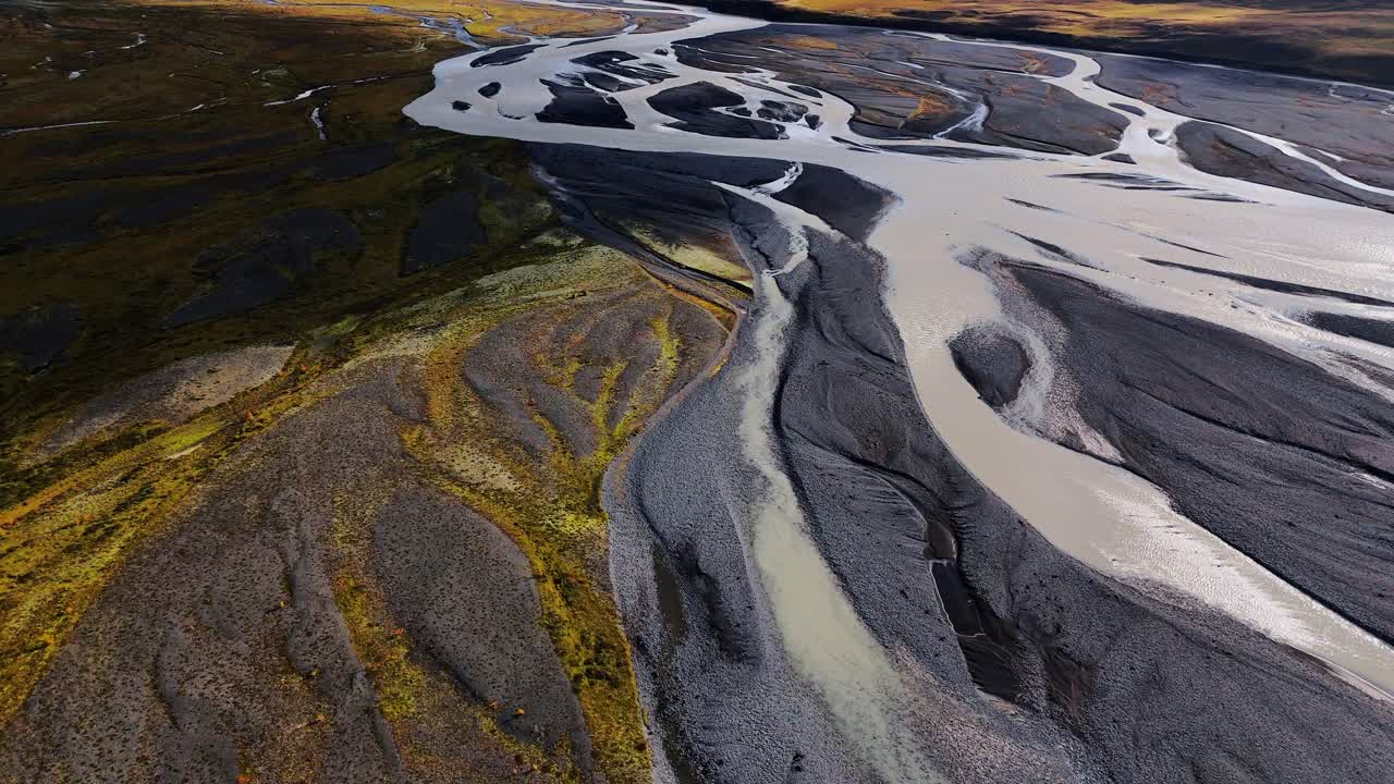 Icelandic streams twist like veins on their journet through glaciated volcanic valleys, volcanic rock and autumnal mossy green flatlands to the sea. Drone aerial fly over