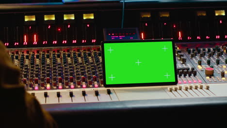 music producer holding a tablet with greenscreen display on mixing console