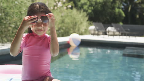 Biracial-girl-with-brown-hair-wears-pink-swimwear-and-heart-shaped-sunglasses