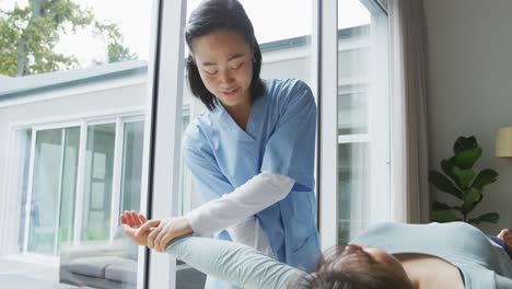 smiling asian female physiotherapist treating arm of female patient lying on bed at surgery